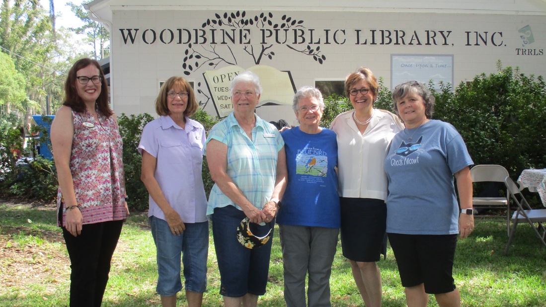 Six people smiling in front of a library sign outdoors.