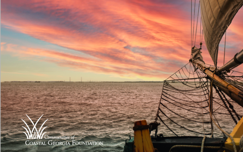 Sailing ship at sunset with pink and orange sky.