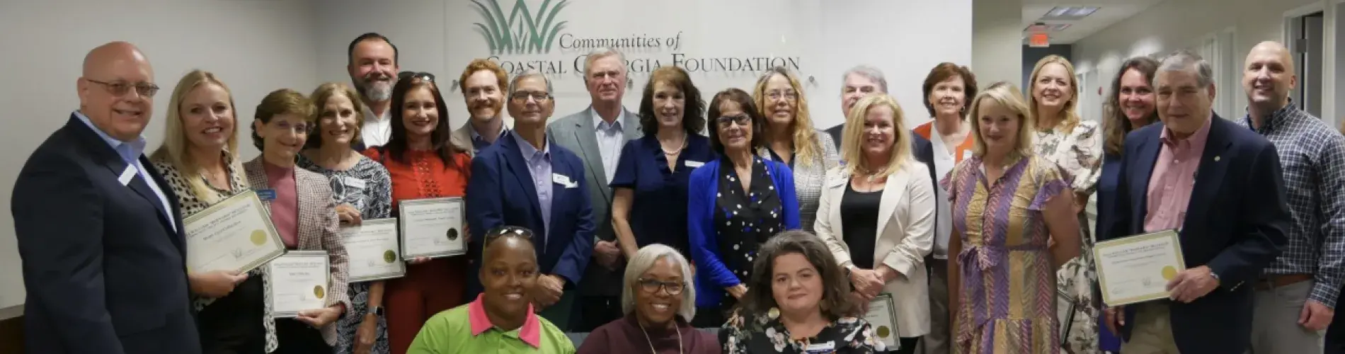 Group of award recipients smiling, holding certificates indoors.