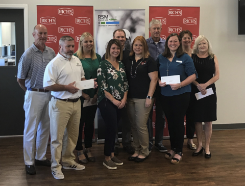 Group of people holding papers, smiling, standing indoors with banners in the background.