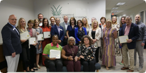Group of award recipients smiling, holding certificates indoors.